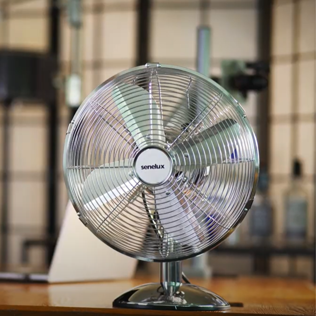 A photo of the new Senelux 12 inch chrome desk fan blowing cool air into a room whilst sat on a desk