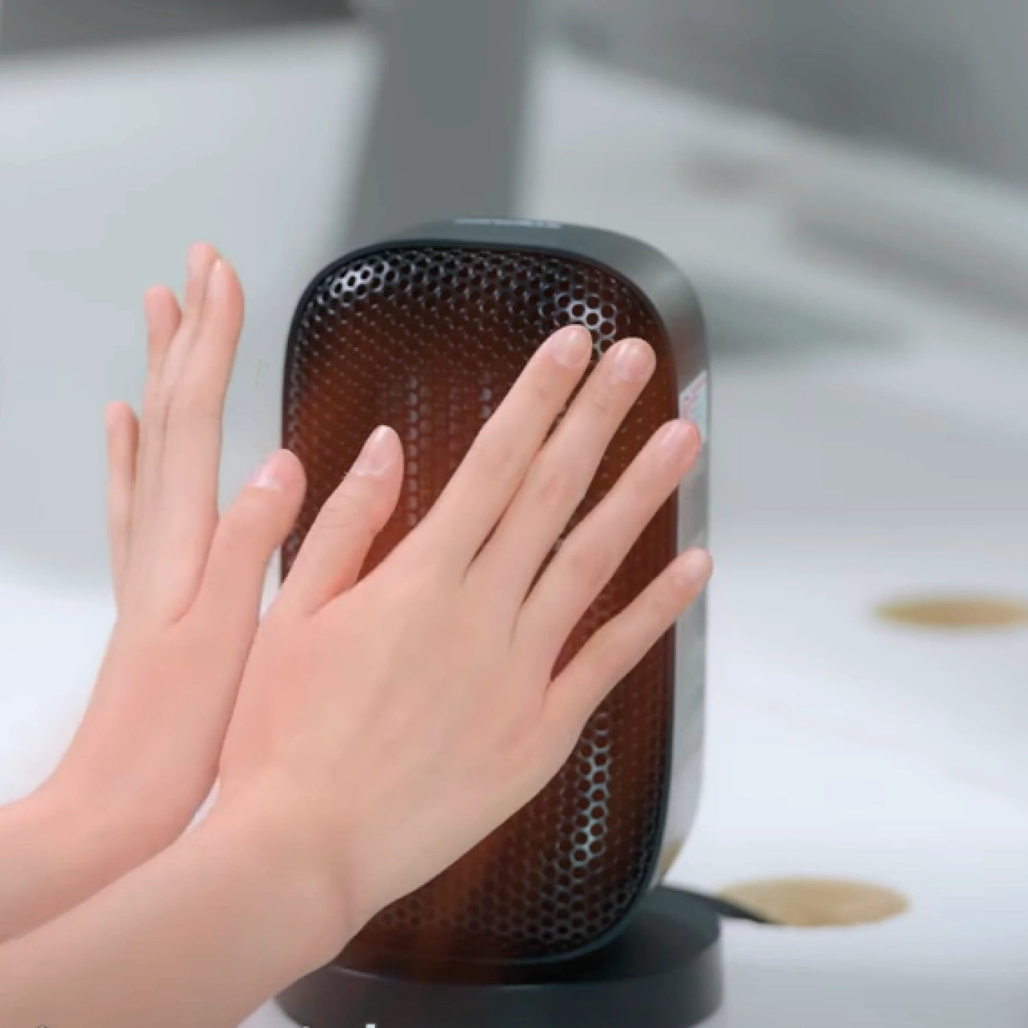 Cold hands being warmed in front of a Senelux Desktop Space Heater which is blowing warm air in an energy efficient way.