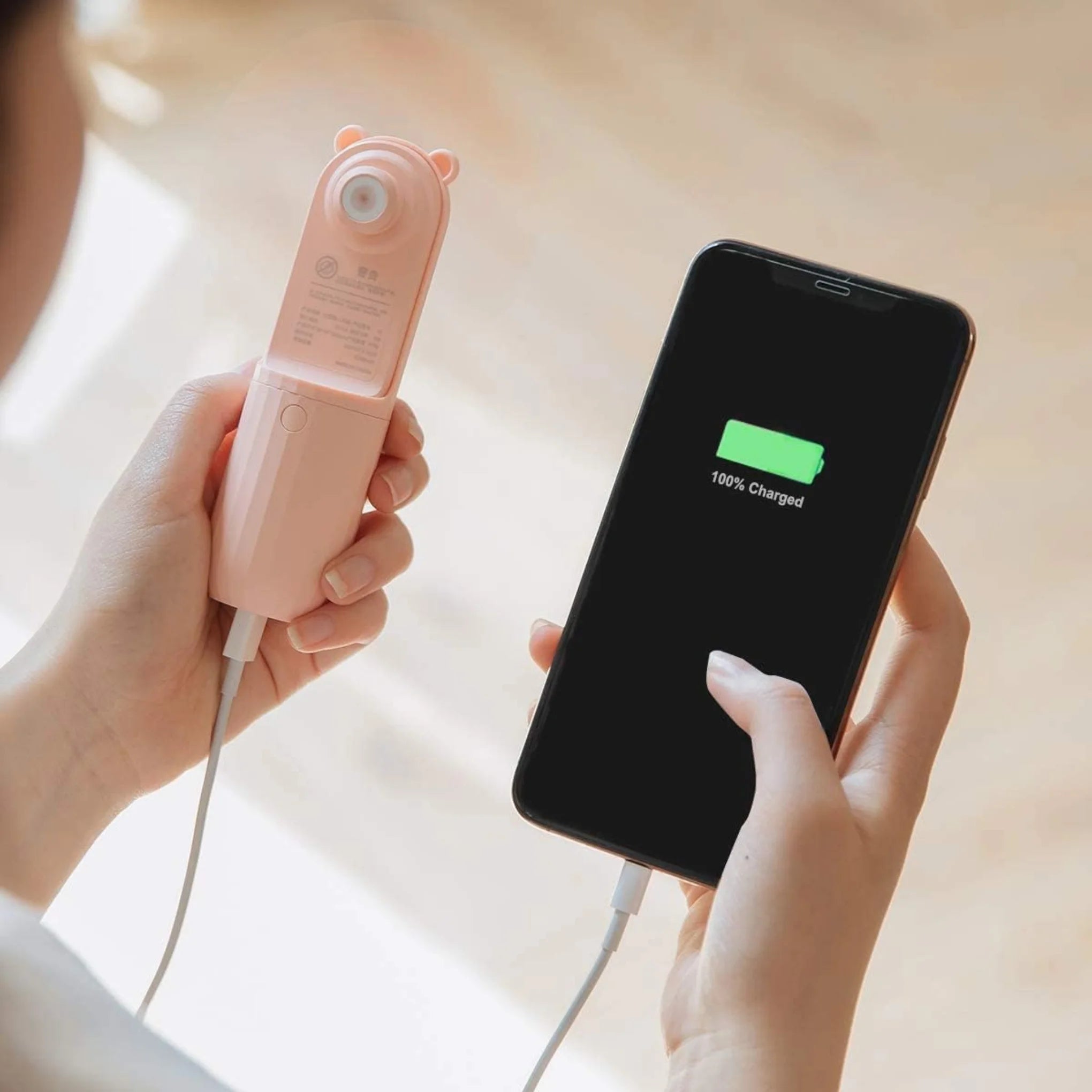 Showing a woman using the pink pocket fan to fully charge her eye phone with the additional power bank feature