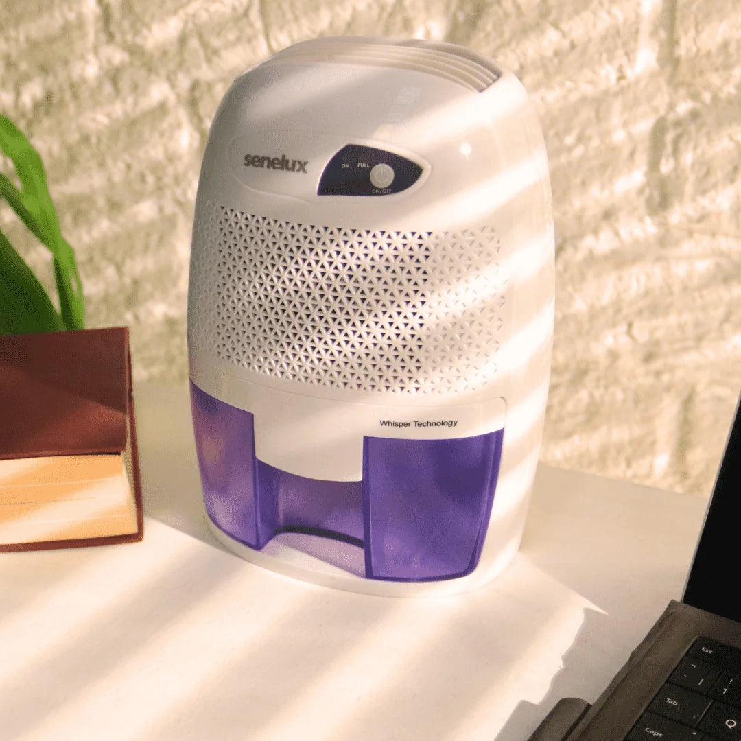 A picture of a Senelux Mini Dehumidifier sitting on an office desk alongside a book and a work laptop