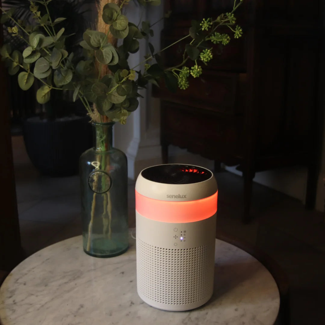 A photo of a Senelux Demi Air Purifier that has an orange LED light shining against a dark background