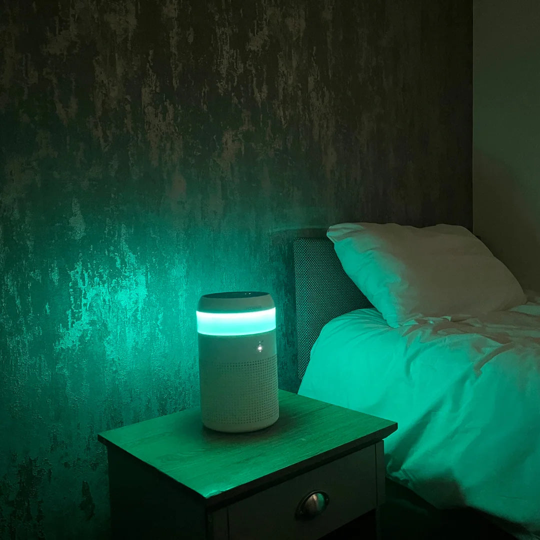 A photo showing the turquoise colour of the LED light inside a Senelux Demi Air Purifier with a bed in the background 