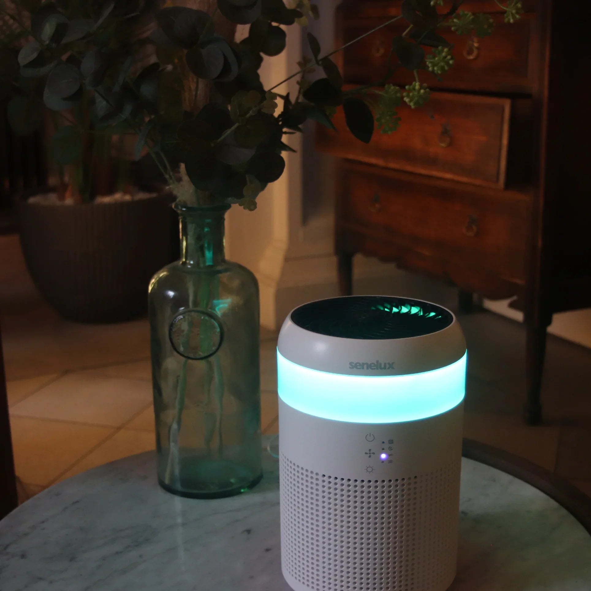 A picture of a Senelux Demi Air Purifier on a marble table with a blue light shining from it's led light strip.