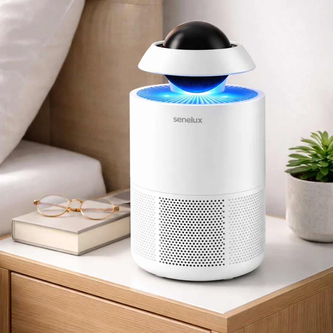 White air purifier with blue light on a wooden table, surrounded by books and a plant.