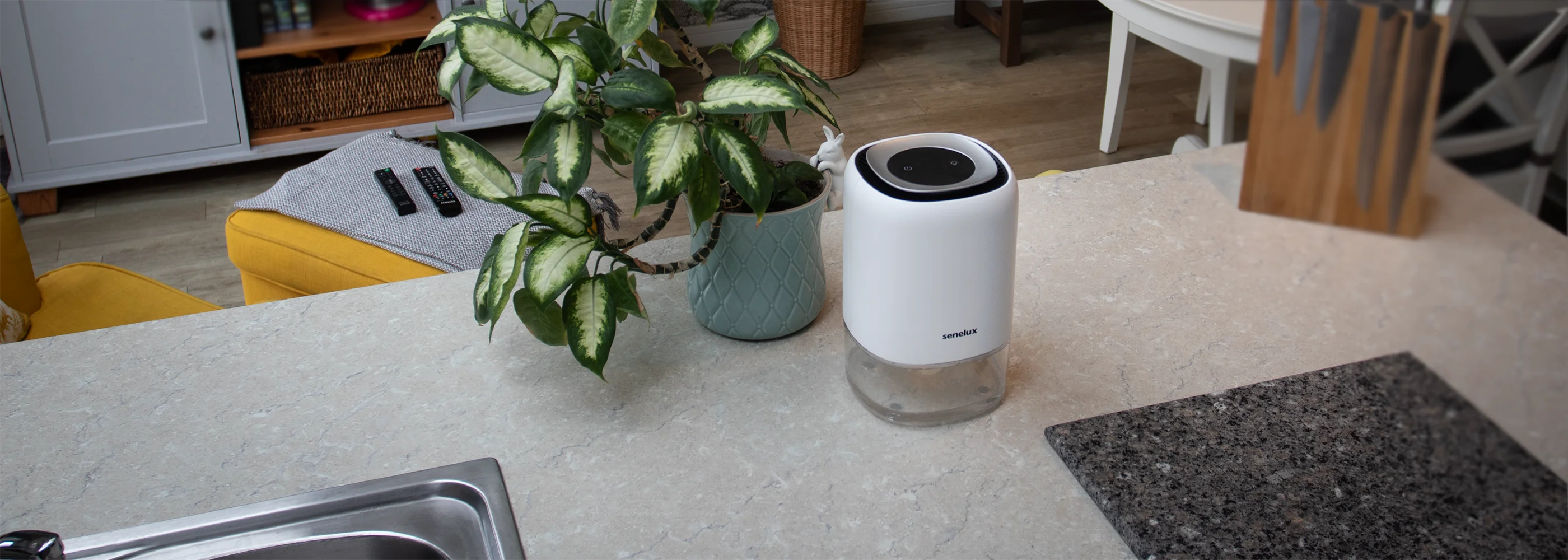 A photo of the Senelux Q4 Dehumidifier in a kitchen setting with a marble chopping board and plant