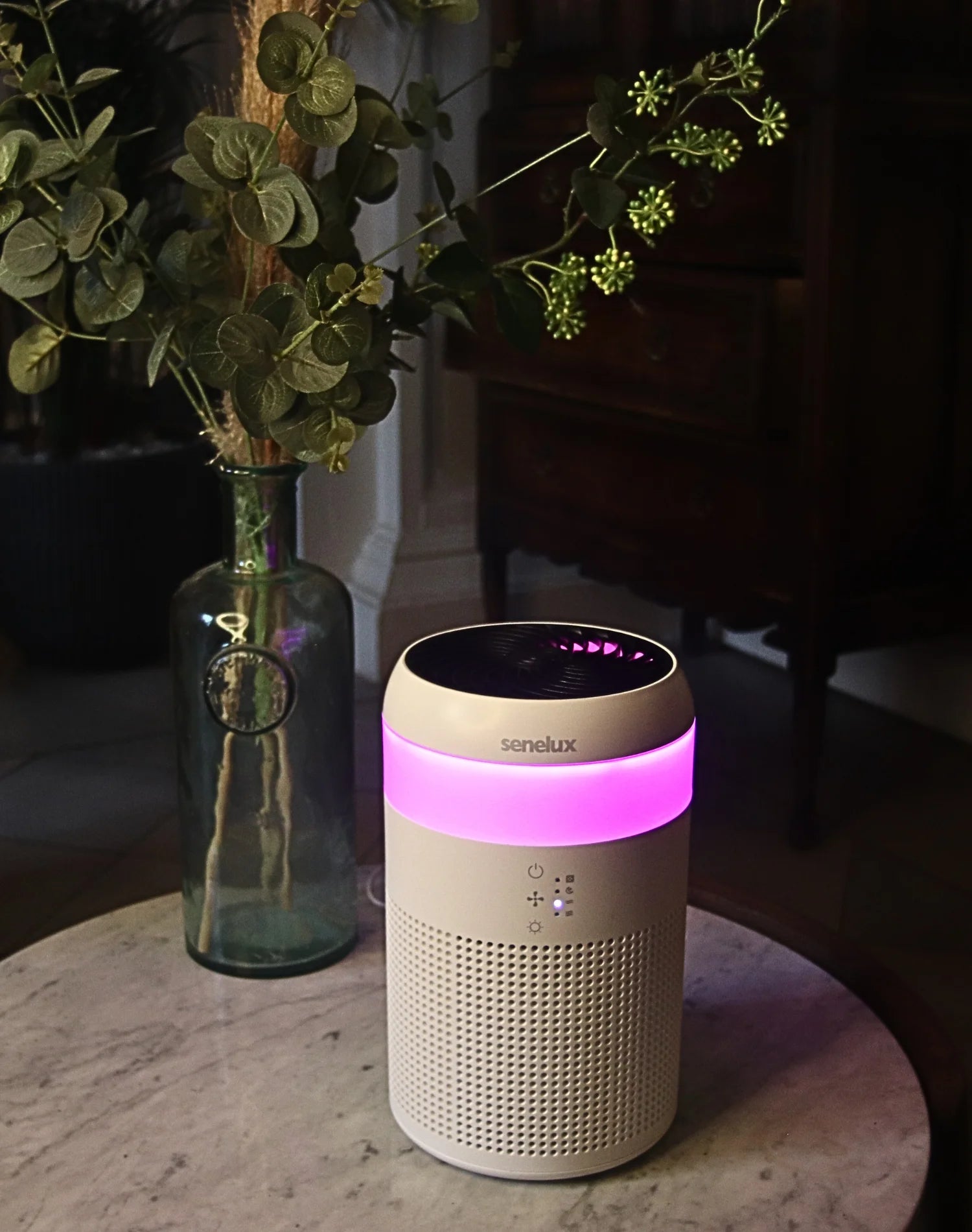 A demi air purifier with a vibrant, pink LED light shining on a marble table with a plant